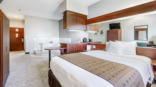 A hotel room with a bed, a desk, a mirror, a TV, and a bathroom with a sink and shower.