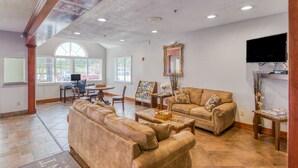 A spacious living room with a large sofa set, a coffee table, and a television mounted on the wall.