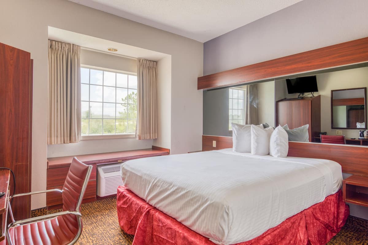 Quarto de hotel com uma cama grande, uma escrivaninha com cadeira, televisão e janela com cortinas.