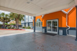 A covered outdoor area with a palm tree, a building with orange walls, and a clear sky.