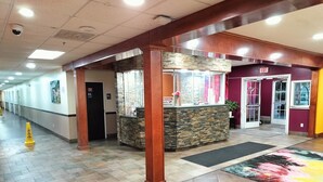 A hotel lobby with a reception desk, a security camera, a fire exit, and a tiled floor.