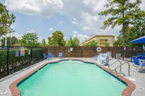 A swimming pool with a wooden fence, blue lounge chairs, and a lifeguard stand.
