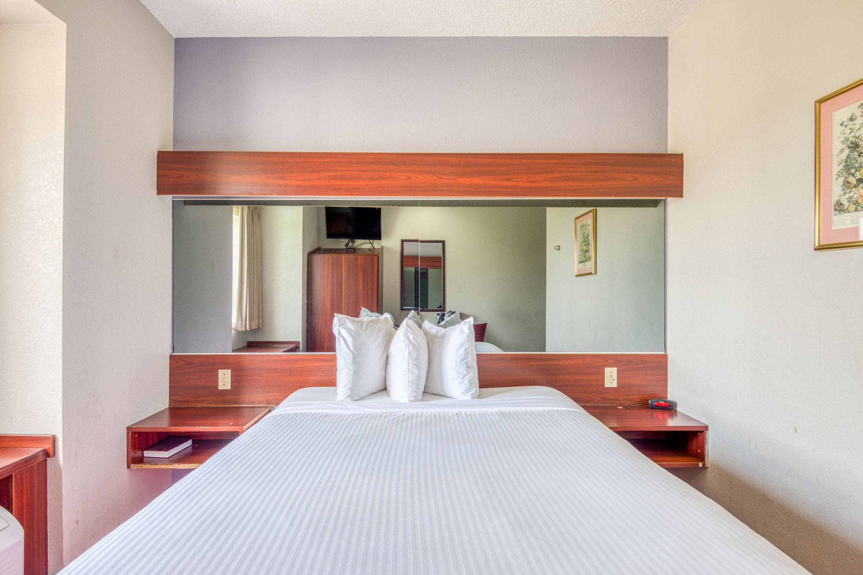 Camera d'albergo con un letto grande, una testiera in legno, uno specchio e un comodino.