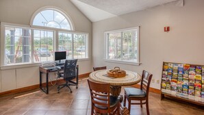 A dining area with a round table, chairs, a computer desk, and a bulletin board with various papers.