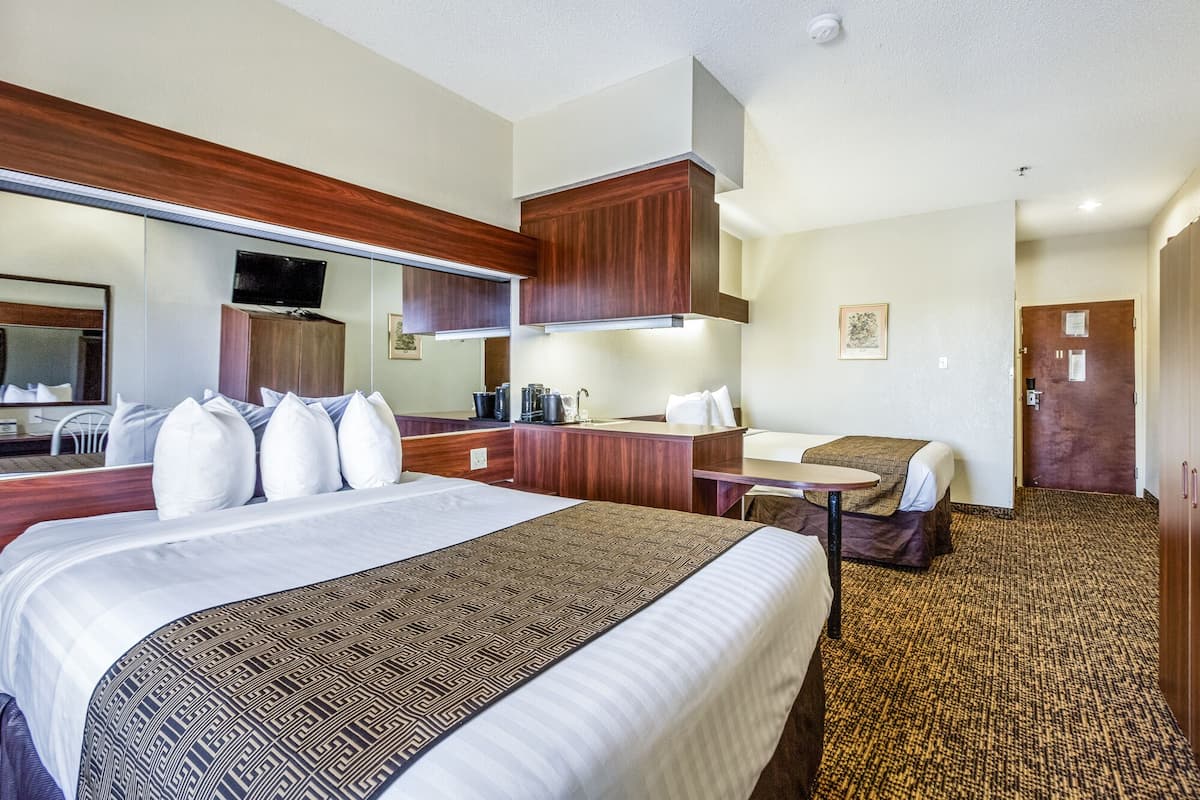Quarto de hotel com uma cama grande, uma escrivaninha, uma cadeira, um espelho e uma porta.