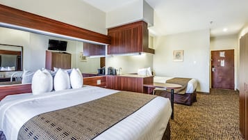 A hotel room with a large bed, a desk, a chair, a mirror, and a door.