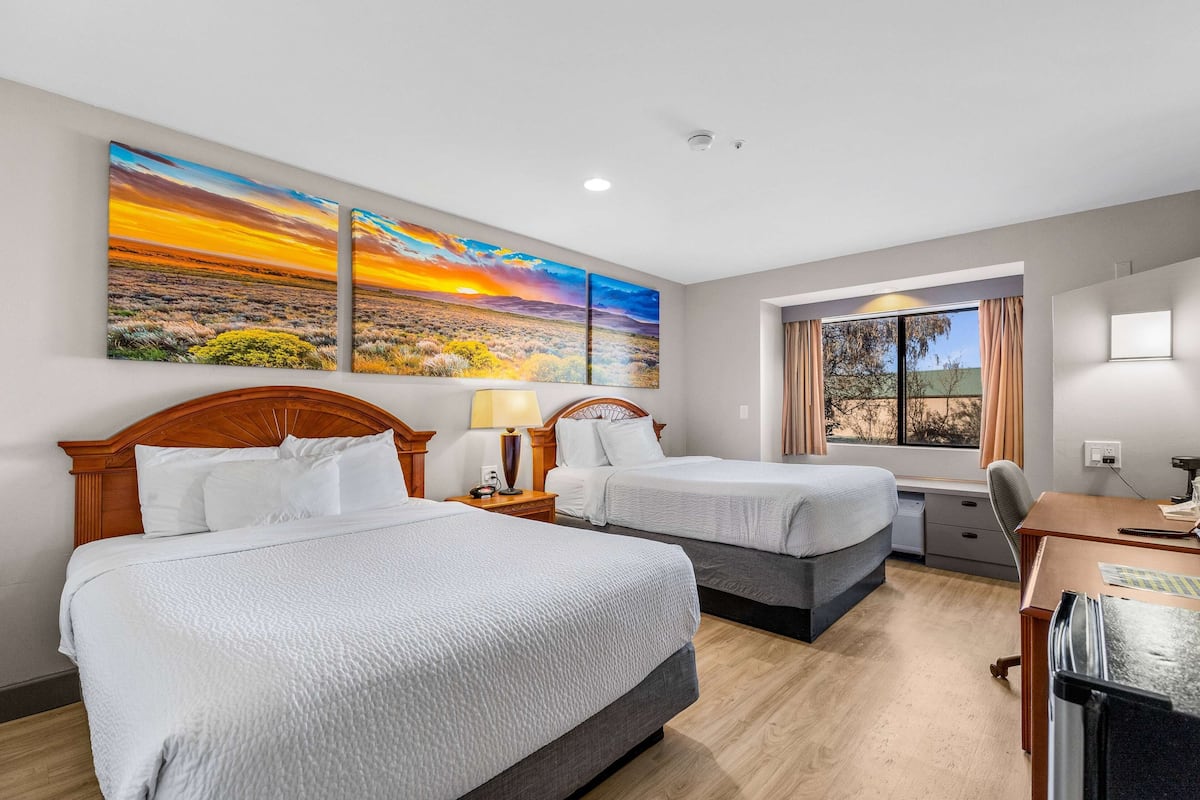 Habitación de hotel con dos camas, un escritorio, una silla y un ventanal con cortinas.
