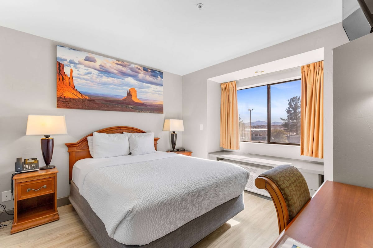 Habitación de hotel con una cama grande, dos mesitas de noche con lámparas, un escritorio y una ventana con cortinas.