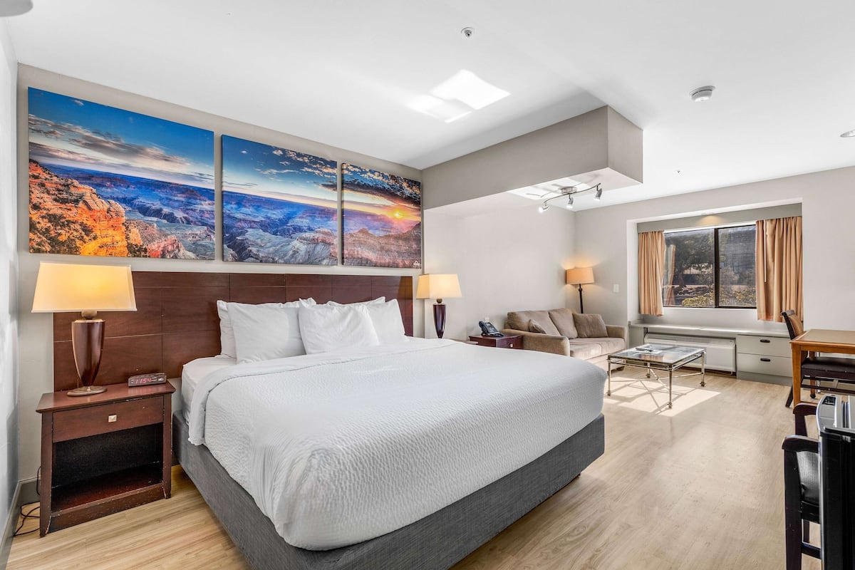 Habitación de hotel con una cama grande, dos mesitas de noche con lámparas, un escritorio, una silla y una ventana con cortinas.
