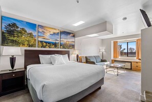 Un hotel moderno con una cama grande, un escritorio con silla, una ventana con cortinas y una obra de arte en la pared.