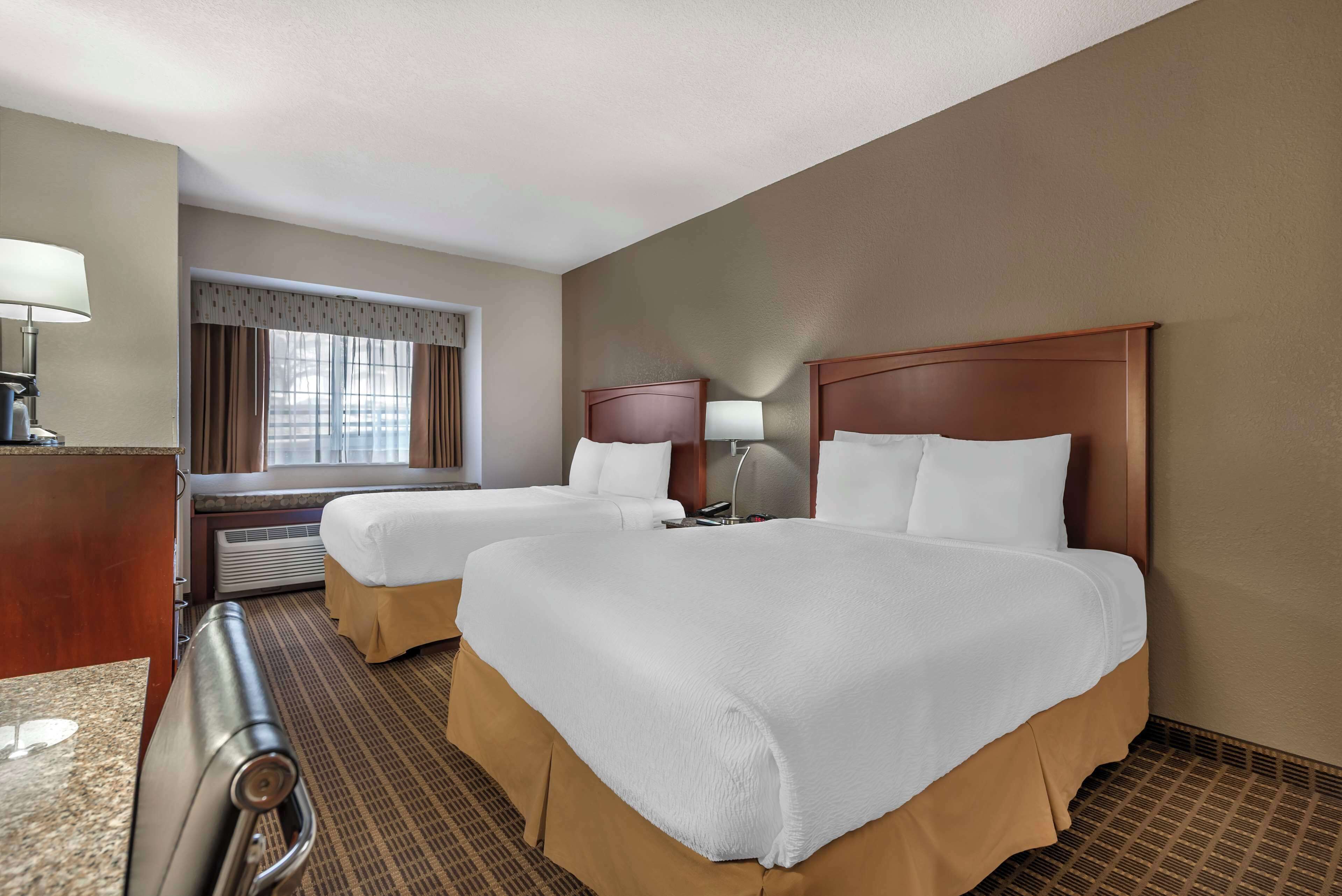 A hotel room with two beds, a desk, a lamp, and a window.
