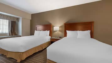 Quarto de hotel com duas camas, uma mesa de cabeceira, uma luminária e uma janela com cortinas.