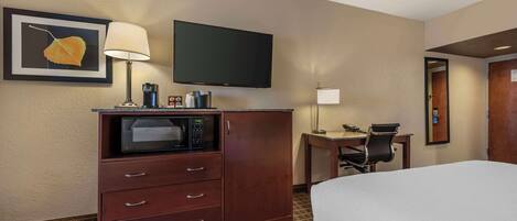 Habitación de hotel con cama, escritorio con silla, microondas, televisión y un cuadro en la pared.