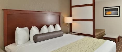 Habitación de hotel con una cama grande, un cabecero de madera, una mesita de noche con lámpara, una pequeña mesa y un cuadro en la pared.