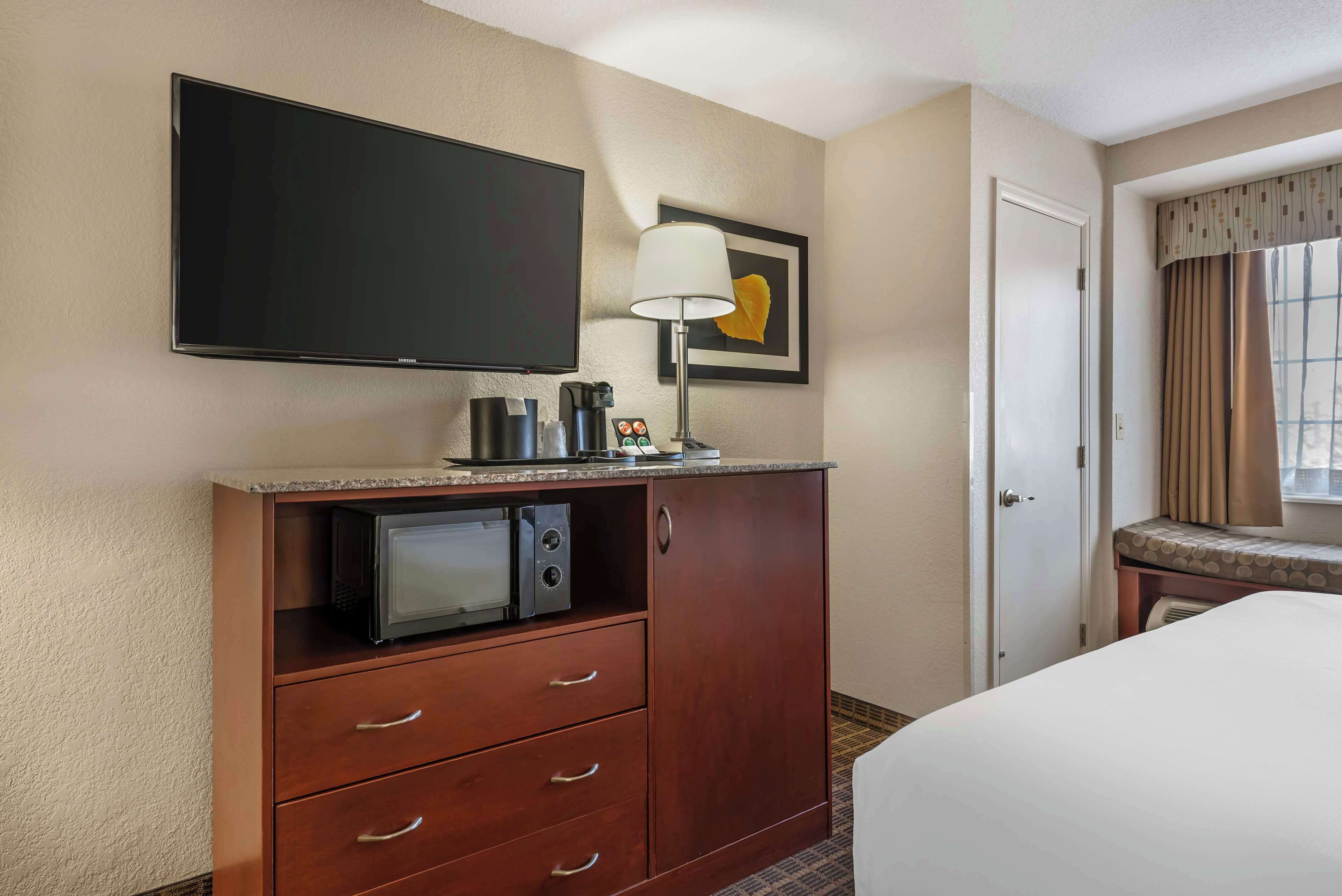 Une chambre d’hôtel équipée d’un téléviseur à écran plat, d’une machine à café, d’un four à micro-ondes, d’un bureau avec une lampe, d’un lit et d’une porte.