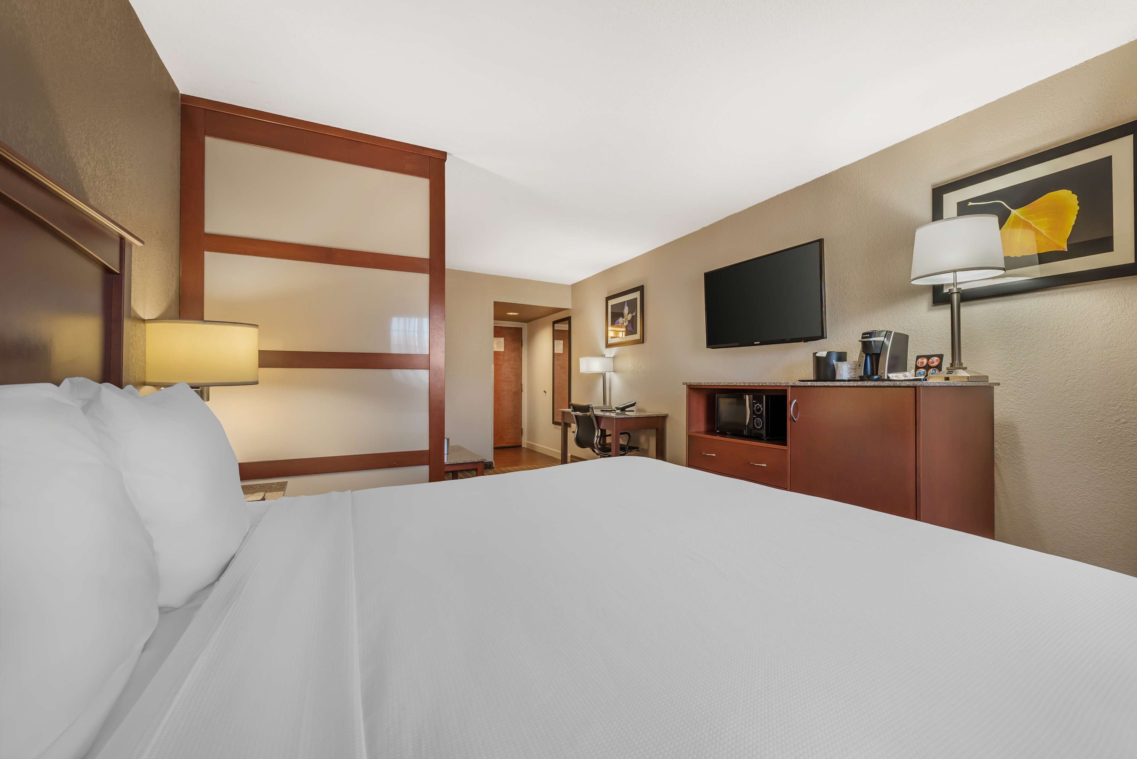 A hotel room with a large bed, a desk, a television, a coffee machine, and a cabinet.