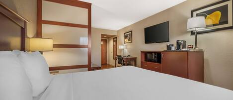 A hotel room with a large bed, a desk, a television, a coffee machine, and a cabinet.