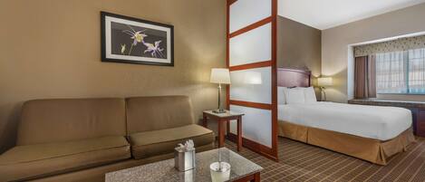 Habitación de hotel con sofá, cama, mesita de noche con lámpara, un cuadro en la pared y ventana con cortinas.