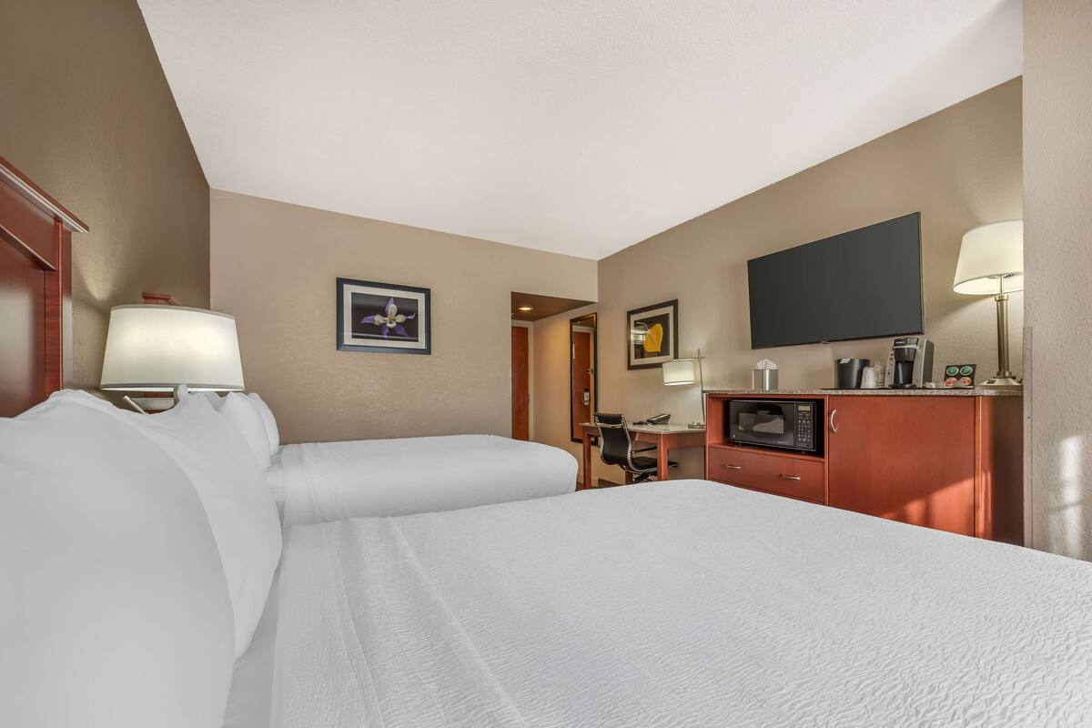 A hotel room with two beds, a desk, a microwave, and a flat-screen TV.