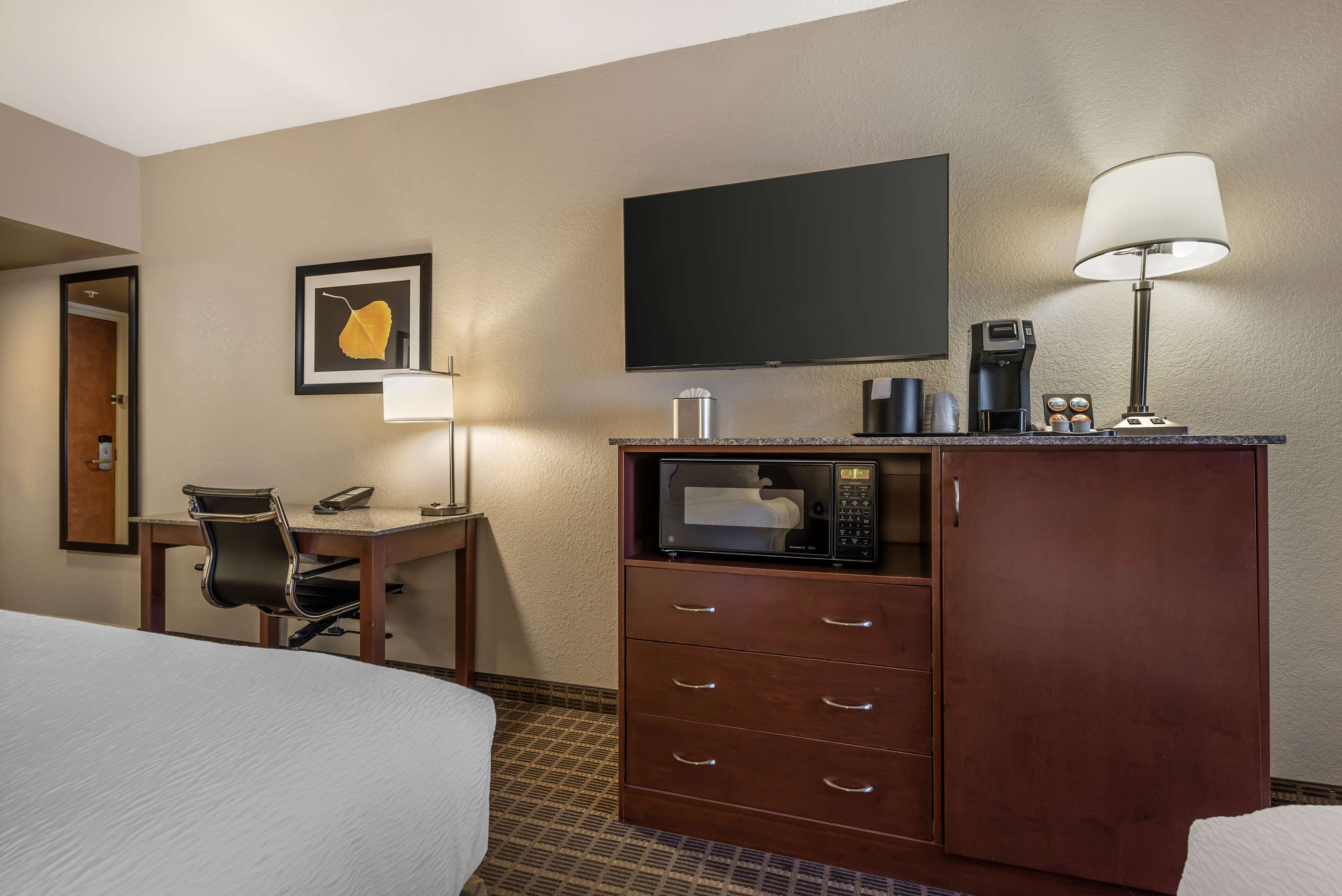Ein Hotelzimmer mit einem Bett, einem Schreibtisch mit Stuhl, einem Flachbildfernseher, einer Kaffeemaschine, einer Mikrowelle und einem Schrank mit Schubladen.
