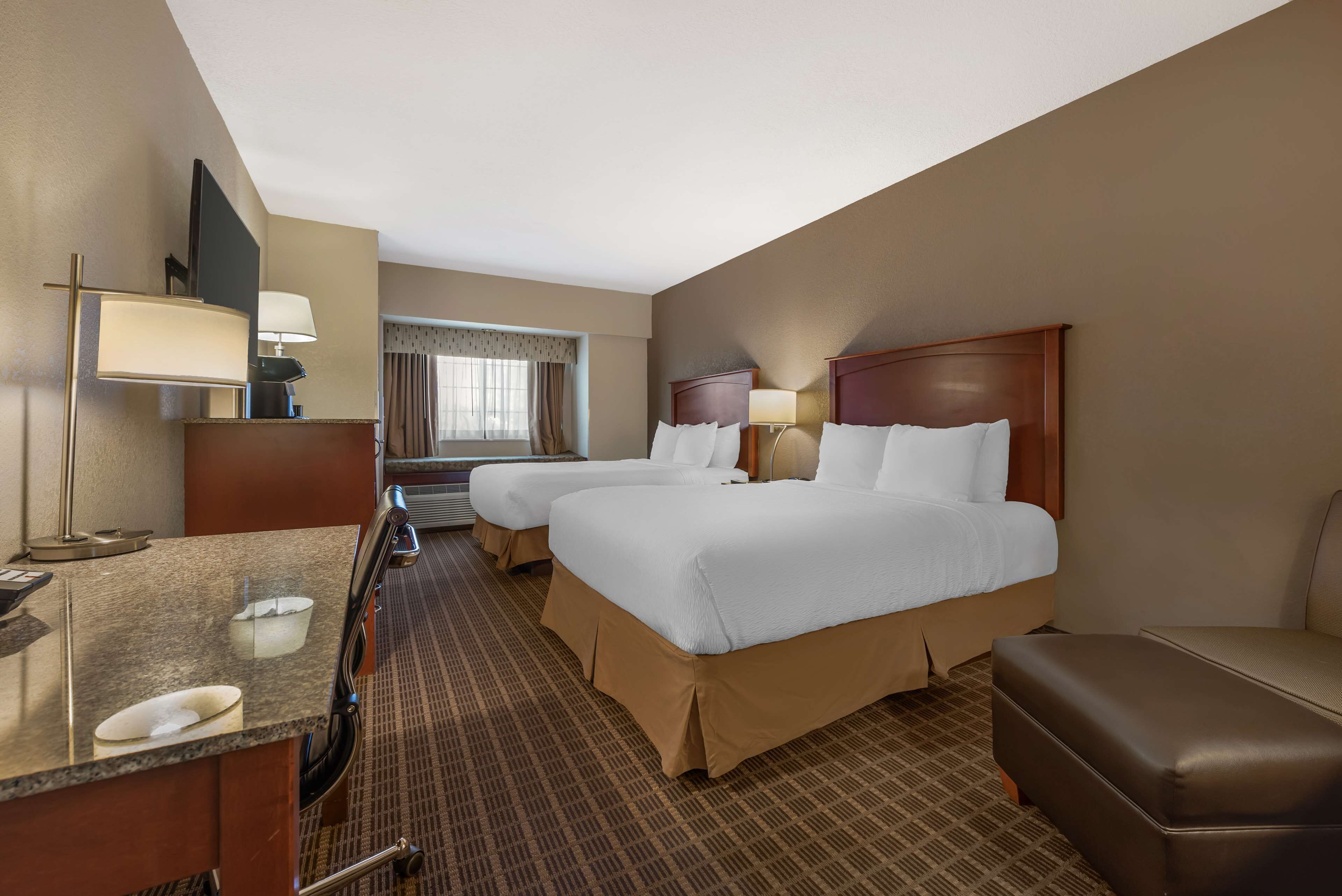 A hotel room with two beds, a desk with a lamp, a TV, and a window with curtains.