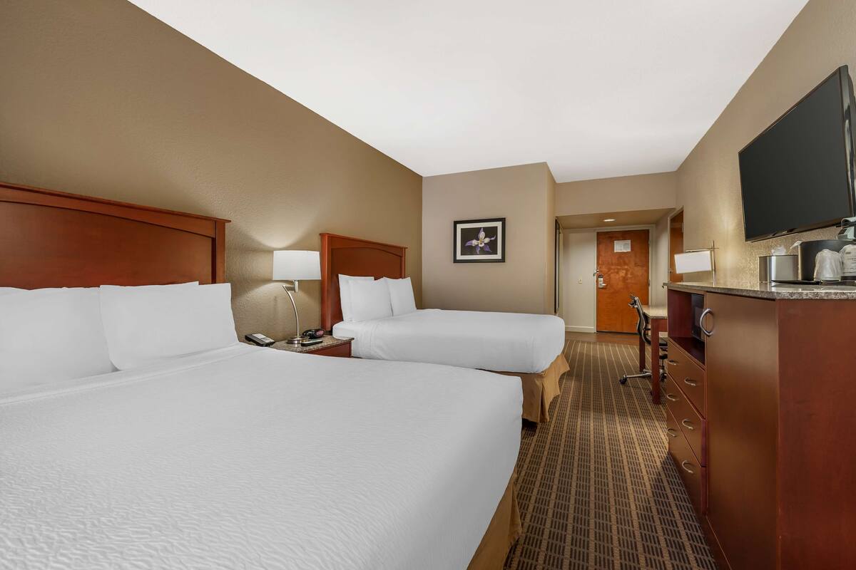A hotel room with two beds, a desk, a TV, and a minibar.
