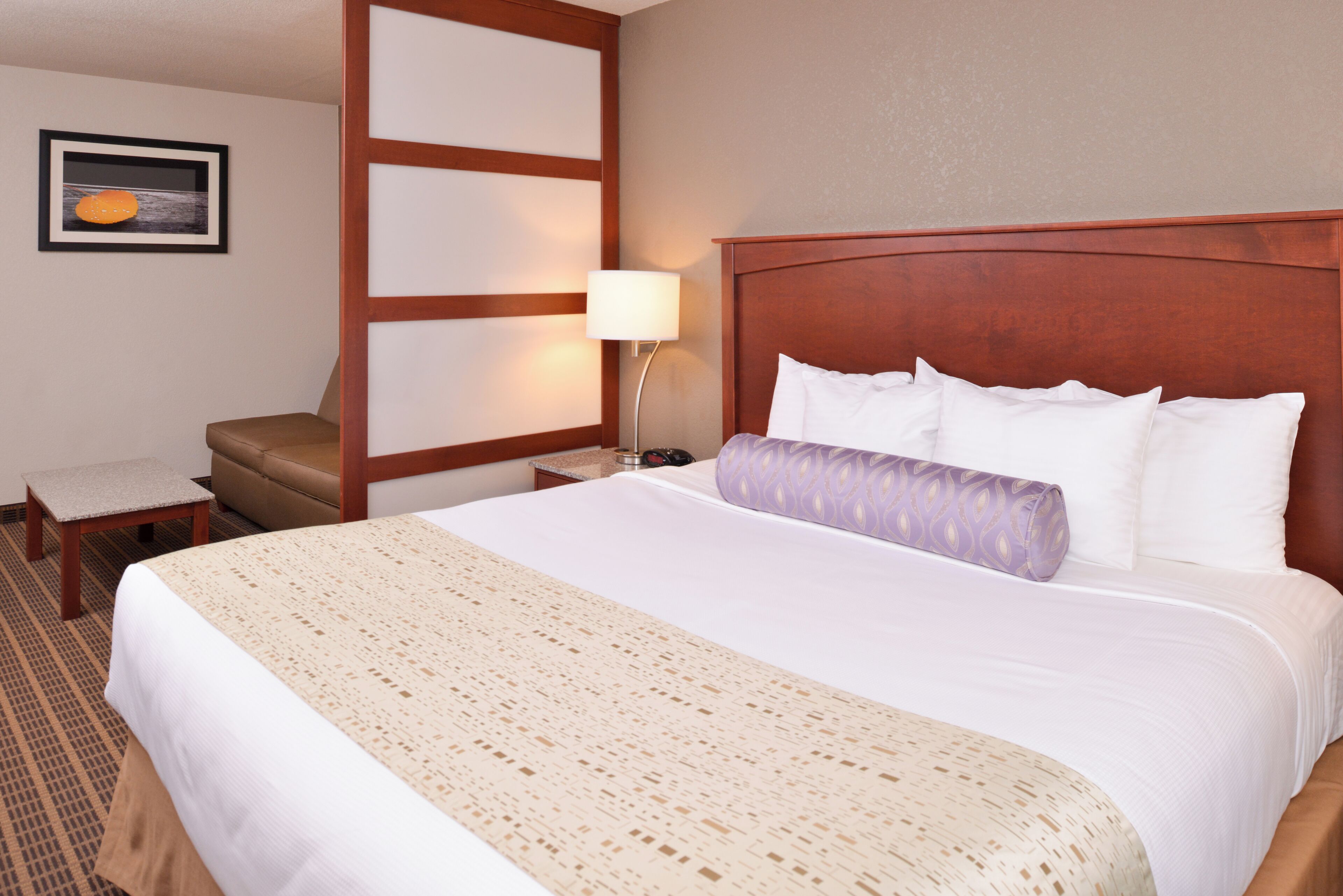 A hotel room with a large bed, a nightstand with a lamp, a chair, and a picture on the wall.