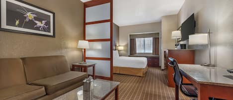 A hotel room with a sofa, a desk, a bed, a TV, and a painting on the wall.