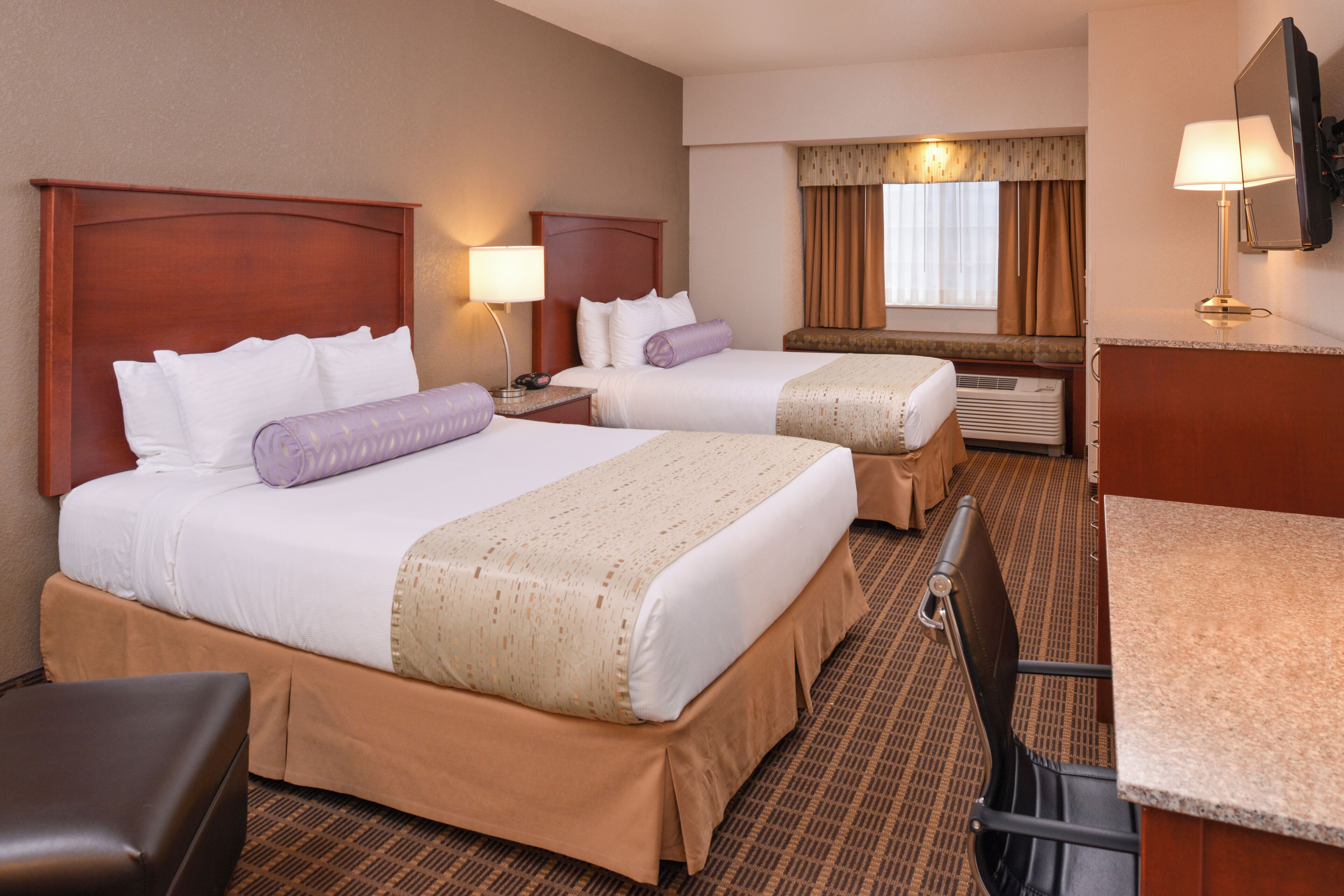 A hotel room with two beds, a desk, a chair, a TV, and a window with curtains.