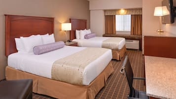 A hotel room with two beds, a desk, a chair, a TV, and a window with curtains.