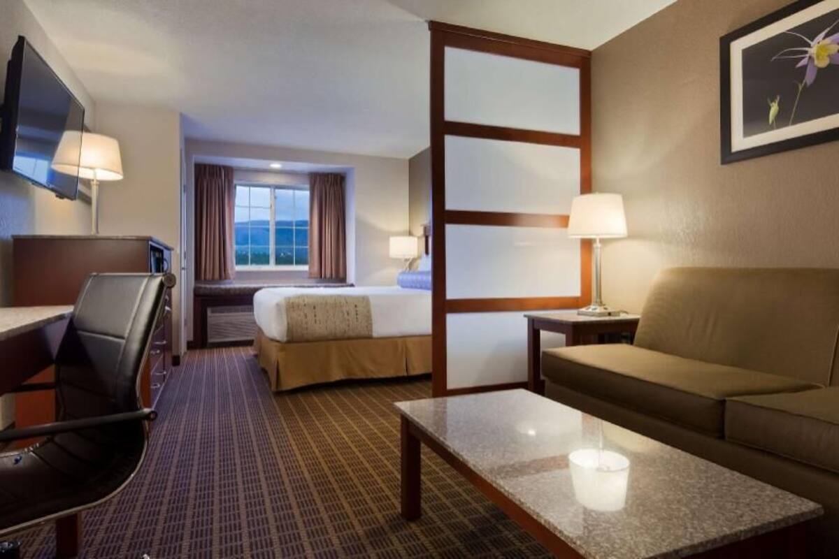 A hotel room with a bed, a sofa, a desk, a chair, a TV, and a window with curtains.