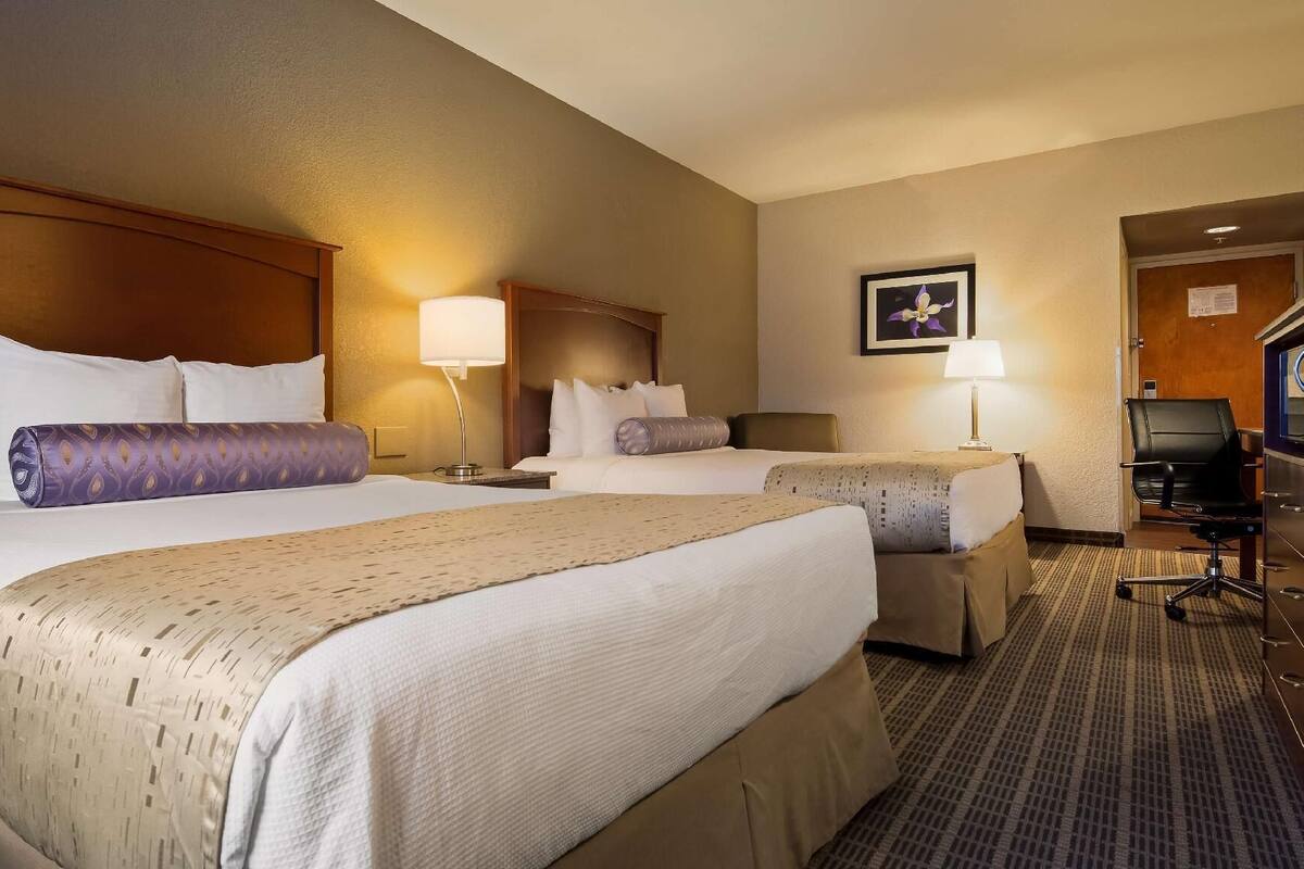 A hotel room with two beds, a desk, a chair, and a television.