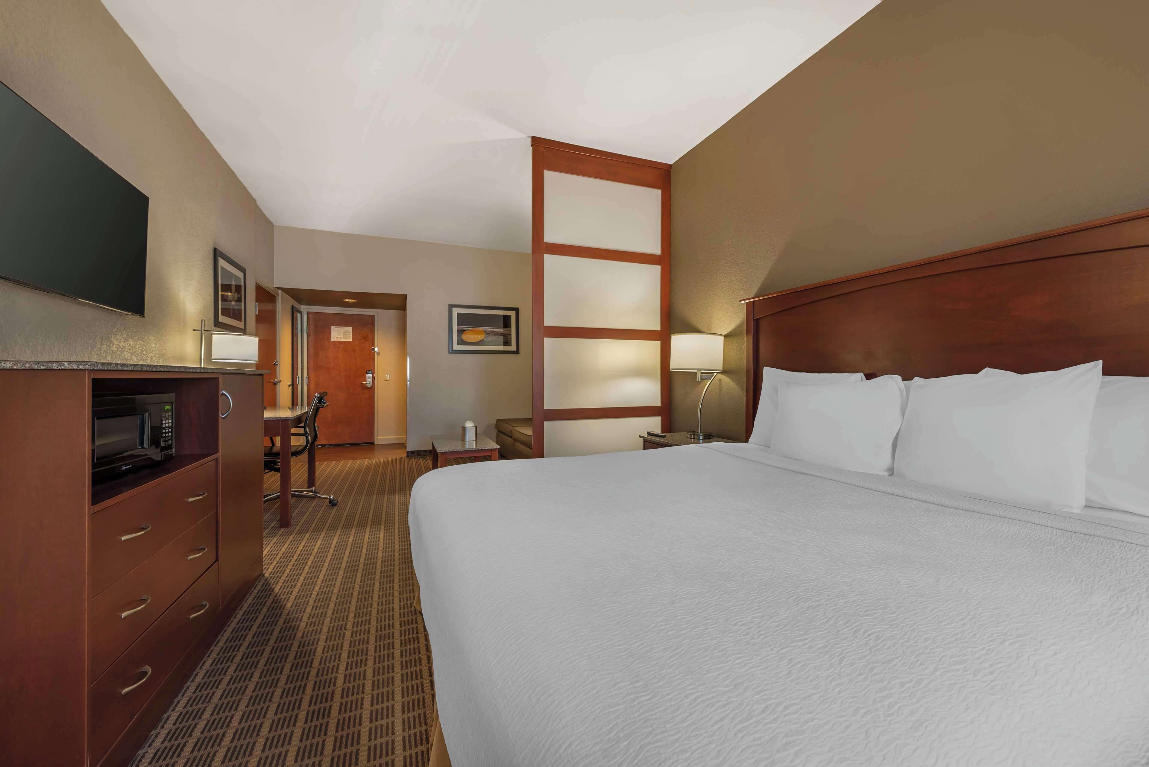 A hotel room with a large bed, a desk with a chair, a television, and a microwave.