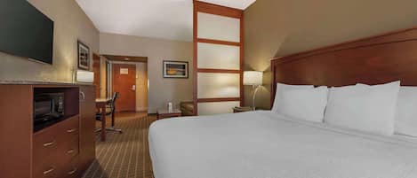A hotel room with a large bed, a desk with a chair, a television, and a microwave.