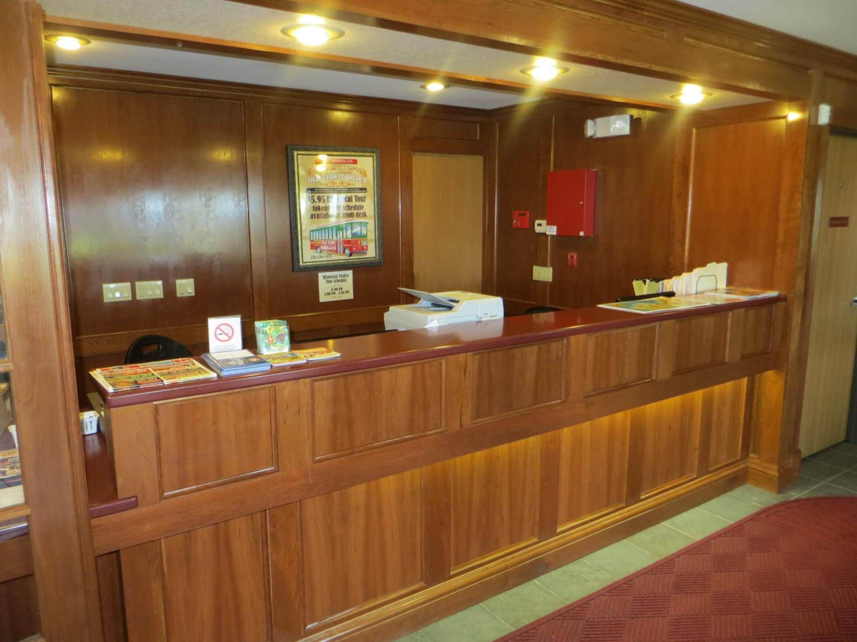 A reception desk with a wooden finish, a framed schedule poster, a red fire extinguisher, and a no-smoking sign.