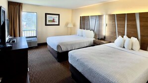 A hotel room with two beds, a desk, a TV, and a window with curtains. - Bayside Hotel of Mackinac (Mackinaw City)
