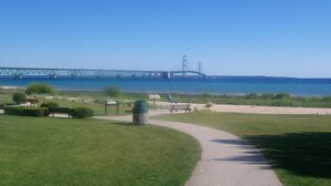 A park with a paved walkway, benches, and a trash can. - Bayside Hotel of Mackinac (Mackinaw City)