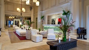 Um hall amplo com balcão de recepção, área de estar com cadeiras brancas e um arranjo de plantas decorativo.
