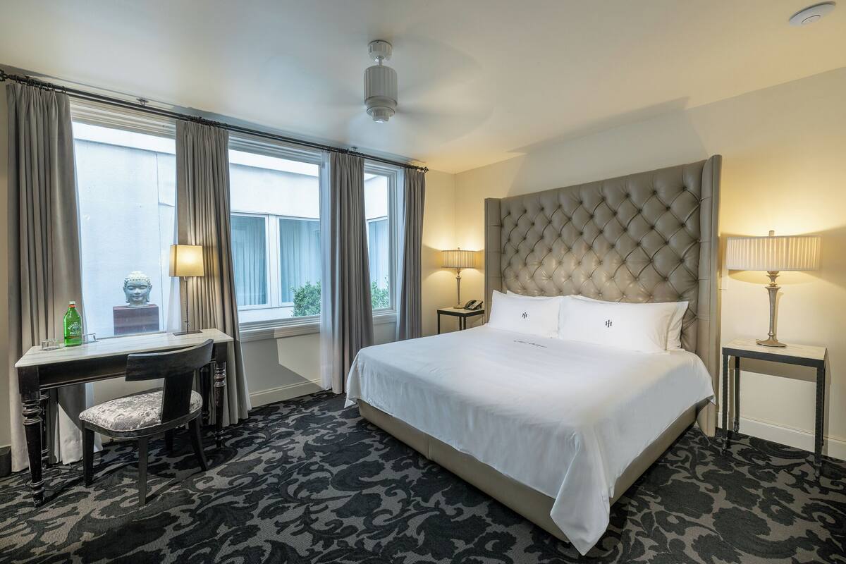 Une chambre d’hôtel avec un grand lit, un bureau avec une chaise, une lampe et une vue sur l’extérieur.