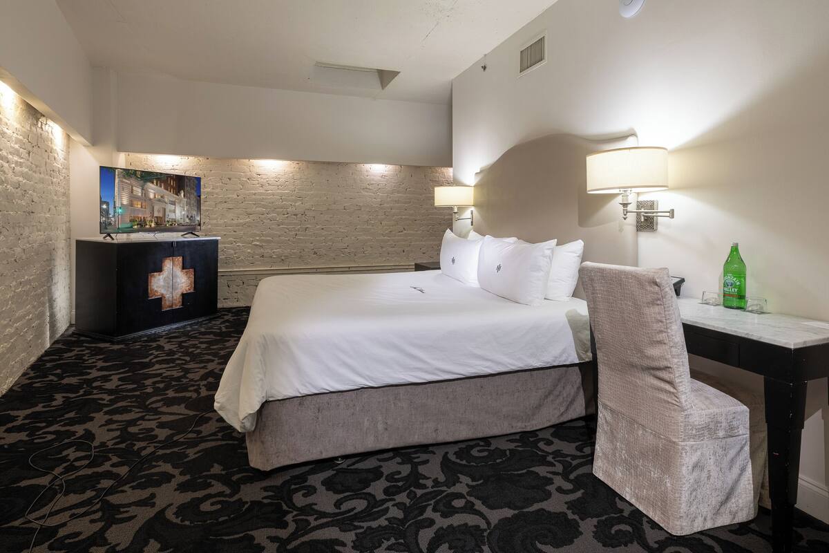 Une chambre d’hôtel avec un grand lit, un bureau, une chaise, une télévision et une lampe fixée au mur.