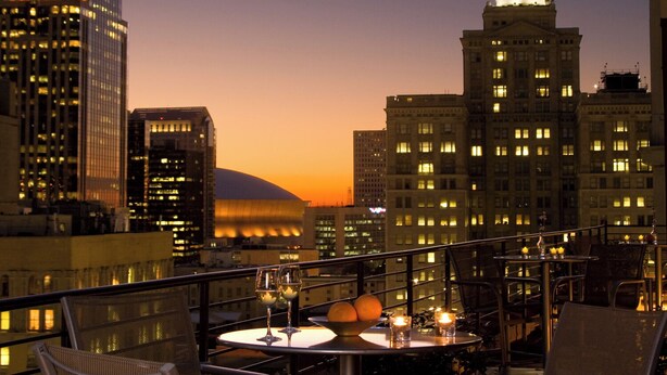 Terraço no terraço com mesa e cadeiras, com vista para o horizonte urbano ao entardecer.