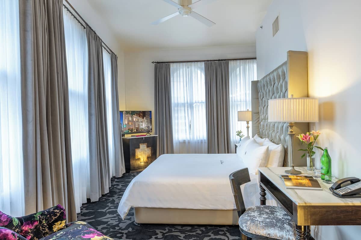 Une chambre d’hôtel avec un grand lit, un bureau avec une lampe, une chaise et un téléviseur posé sur un meuble.