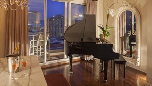 Um piano de cauda em uma sala ampla, com uma grande janela que dá para a paisagem urbana ao entardecer.