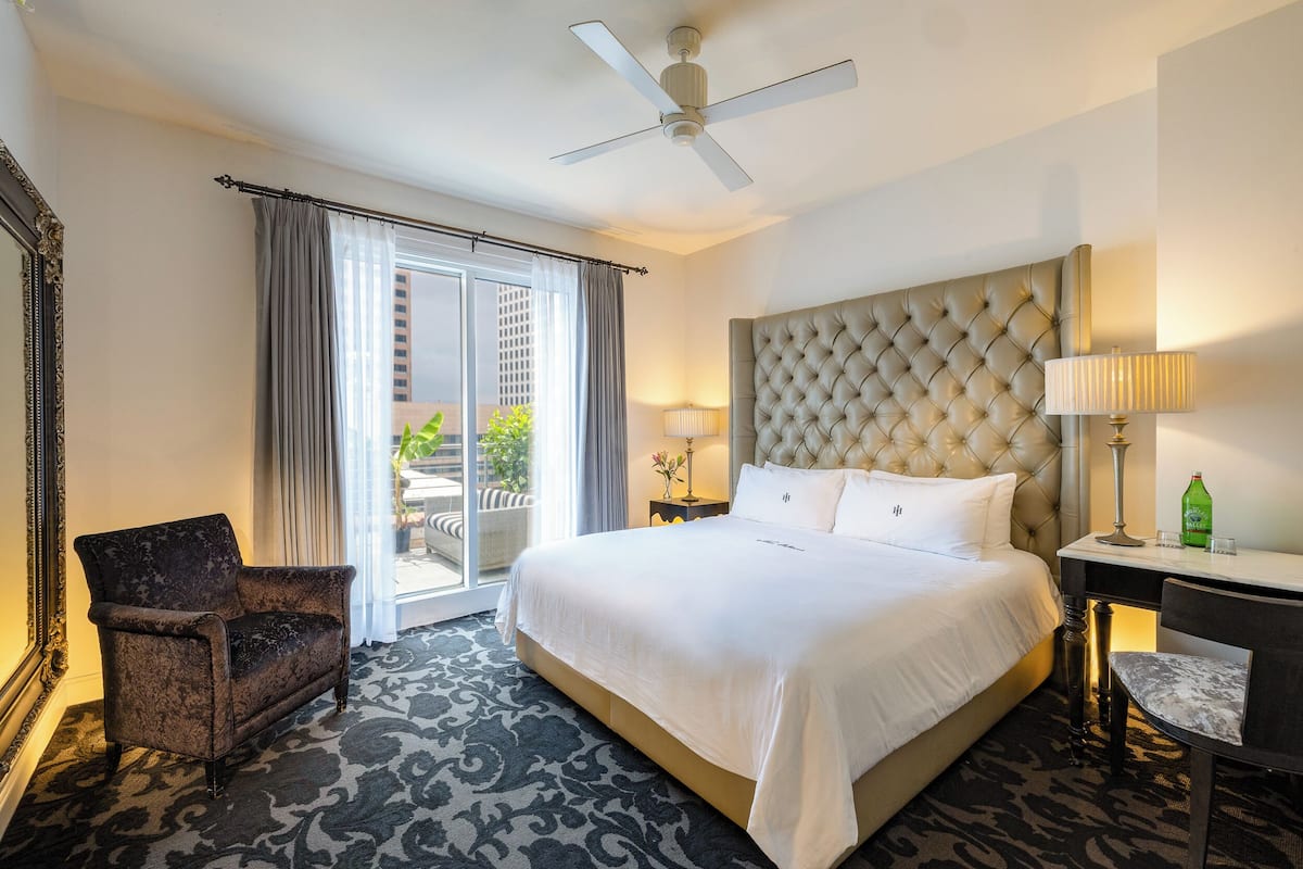 Une chambre d’hôtel avec un grand lit, une chaise, un bureau, une lampe et un ventilateur de plafond.