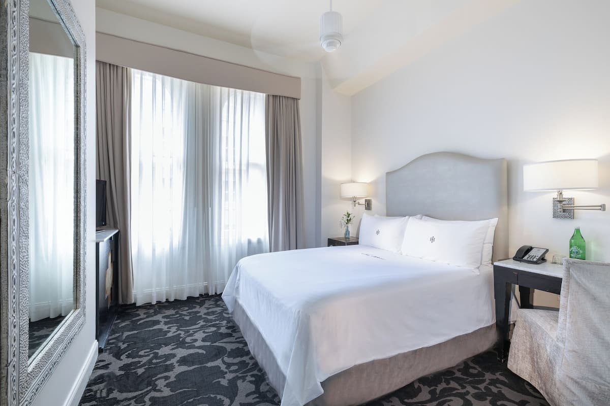 Une chambre d’hôtel avec un grand lit, une table de chevet avec une lampe, un téléphone et un miroir.