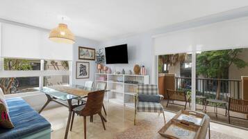 Een moderne woonkamer met een bank, stoelen, een televisie en een balkon met tuinmeubilair.