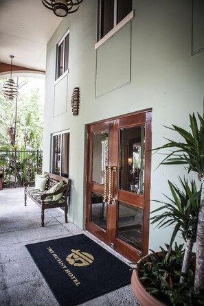 Entrada de un hotel con puerta de madera, un banco y felpudo.