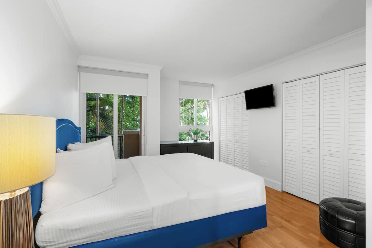 Un dormitorio con cama, televisor montado en la pared y ventana con vista a la vegetación.