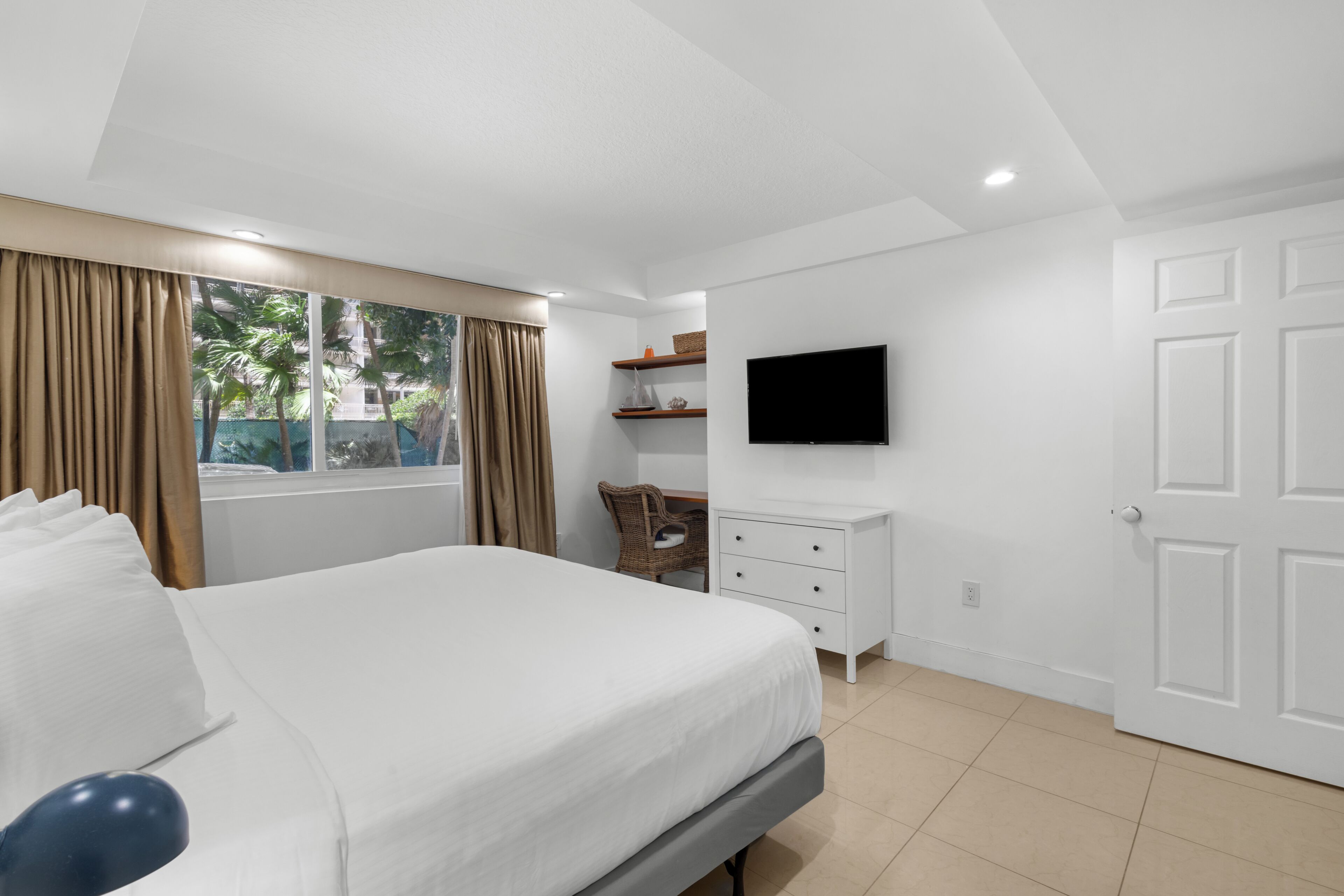 A hotel room with a bed, a TV, a dresser, and a window with curtains.