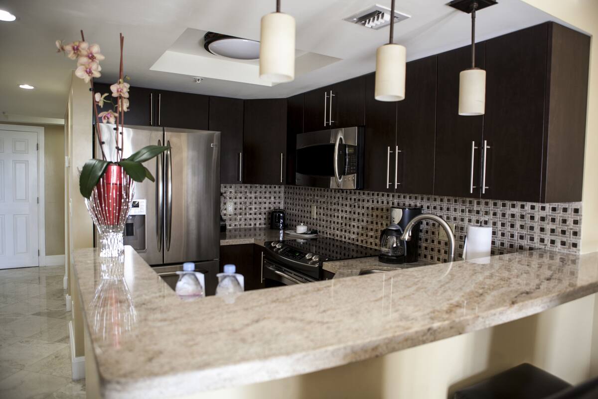 A modern kitchen with dark cabinetry, stainless steel appliances, and a marble countertop.